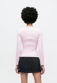 Top rosa de manga comprida com textura canelada, design justo e textura suave, combinado com uma minissaia preta de ganga com bolsos e bainha reta.