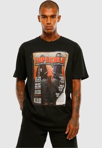Sort bomulds T-shirt med et frontprint, der ligner et magasincover med fed tekst og billeder relateret til hip hop-kultur.