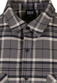 Grijze flanellen shirt met zwart-wit ruitpatroon. Met een puntige kraag, knoopsluiting en borstzak. Inclusief zwarte knopen.