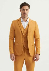 Costume jaune moutarde avec une coupe ajustée, comprenant une veste à un bouton, des revers crantés et un gilet à trois boutons. Texture douce.