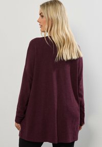 Burgunderröd oversized tröja, mjuk textur, långa ärmar, rundad nederkant och detaljerad söm bak. Lämplig för lager-på-lager-outfits.