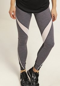 Szare legginsy sportowe o teksturowanym wykończeniu, z zaokrąglonymi akcentami w jasnoróżowym i czarnym kolorze. Projekt podkreśla smukły krój.