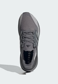 Grå atletisk sko med åndbart mesh-overdel, teksturerede detaljer og fremtrædende snøresystem. "ULTRABOOST" branding synlig på indersålen.