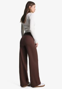 Brown wide-leg pants made of soft fabric, featuring a high waist and a smooth texture. Paired with a fitted white long-sleeve top.