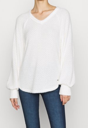 Weißer gestrickter Pullover mit V-Ausschnitt, Raglanärmeln, lockerer Passform und gerippten Bündchen, aus weichem, strukturiertem Material.