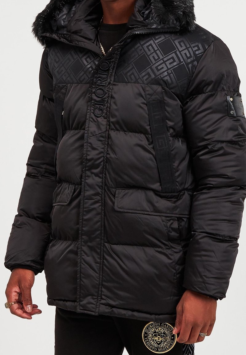 Schwarze Steppjacke mit einer mit Kunstfell besetzten Kapuze, gestepptem Design, Logo-Details auf der Brust und zwei vorderen Taschen mit Reißverschluss.