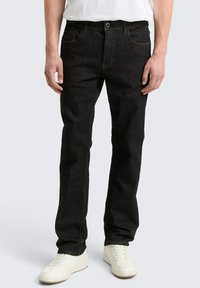 Schwarze Jeans aus Denim mit geradem Bein, Fünf-Taschen-Design und Metallknopfverschluss, kombiniert mit weißen Turnschuhen.