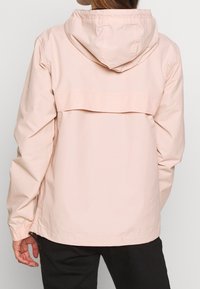 Jasnoróżowa kurtka z kapturem o luźnym kroju, z elastycznymi mankietami i fasonem na plecach. Wykonana z gładkiego, lekkiego materiału.