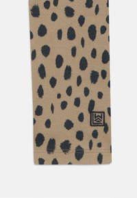 Tessuto beige con texture a righe, caratterizzato da macchie leopardate blu scuro. Include un piccolo logo ricamato nell'angolo.