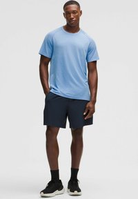Hellblaues strukturiertes Sport-T-Shirt mit kurzen Ärmeln, kombiniert mit dunkelblauen Shorts. Modell trägt schwarze Sneakers und Knöchelsocken.