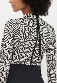 Černo-bílý dlouhý neopren s vzorem a vysokým límcem, s geometrickými designy a zipovým zapínáním na zádech.
