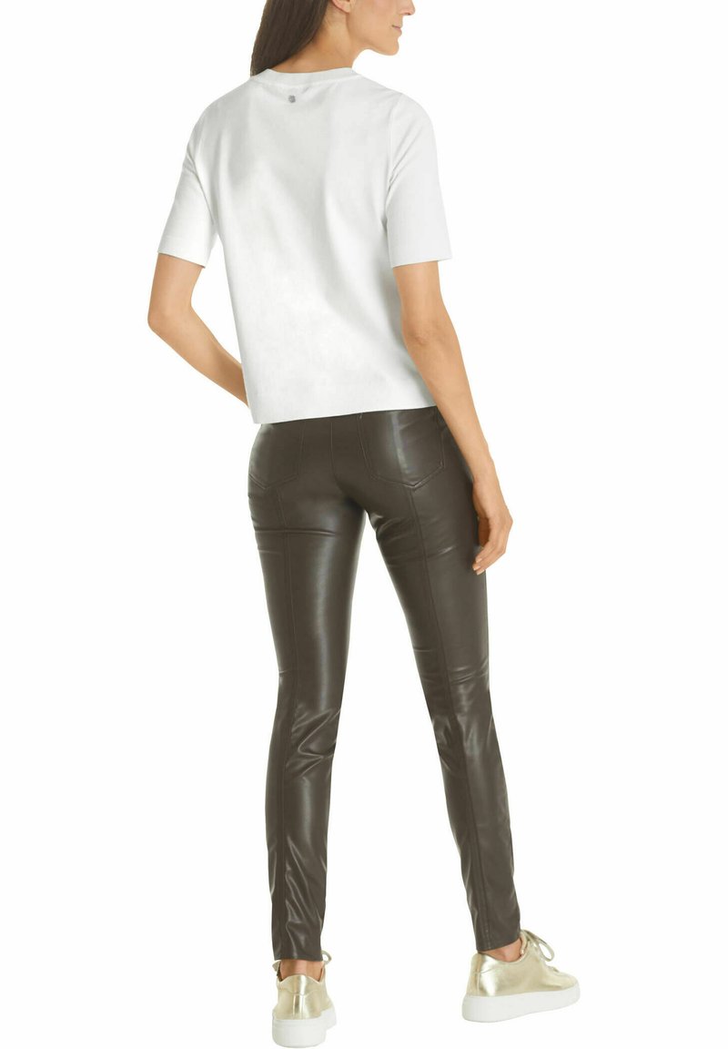 Weißes Kurzarmoberteil mit rundem Halsausschnitt, kombiniert mit eng anliegenden braunen Kunstlederhosen und metallisch goldenen Sneakern. Glatte Textur im gesamten Outfit.