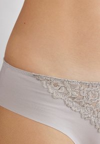 Grå lingerie med en slät tygkropp och en spetskant upptill, prydd med blommönster och vågiga kanter.