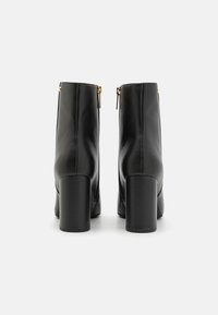 Čierne kožené členkové topánky s hladkým povrchom, vysokými blokovými podpätkami a zlatými zipsovými detailmi na zadnej strane. Jednoduchý, elegantný dizajn.