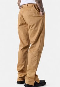 Khaki pants made of cotton, featuring a relaxed fit, elastic waistband, back pocket, and slightly tapered legs. Black footwear is visible.