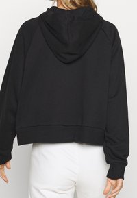Sudadera corta negra con una gran capucha, puños y dobladillo acanalados, hecha de una tela suave con una textura lisa. Diseño simple y versátil.