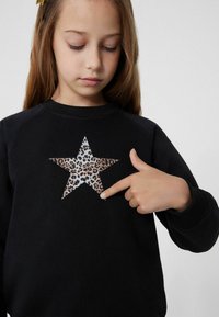 Černá mikina s velkou hvězdou s leopardím potiskem. Textilie vypadá měkce a výstřih je ve stylu crew.