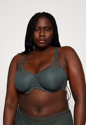 Soutien-gorge vert foncé avec panneaux en mesh, texture géométrique et bretelles réglables. Il possède une fermeture centrale à crochet et des bonnets doux.