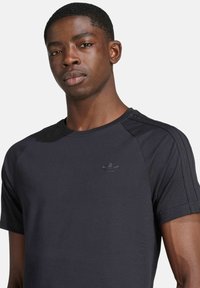 Čierne bavlnené tričko s okrúhlym výstrihom, krátkymi rukávmi, jemnými rebrovanými detailmi a malým vyšitým logom na hrudi.