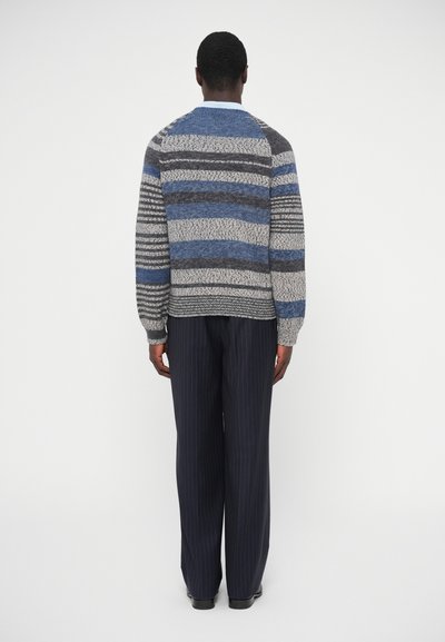 Πλεκτό πουλόβερ με οριζόντιες ρίγες σε γκρι, μπλε και μαύρο, με ριμπ μανσέτες και στρογγυλή λαιμόκοψη, συνδυασμένο με ναυτικό παντελόνι με λεπτές ρίγες.