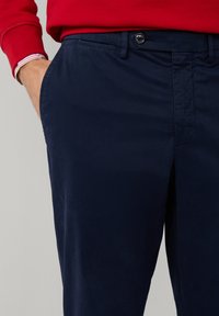 Chinos azul marino hechos de algodón suave, con un diseño de frente plano, bolsillos laterales y cierre de botón en la cintura. Diseño y acabado clásico.