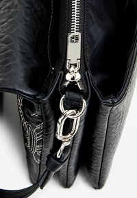 Borsa a mano in pelle nera con superficie testurizzata, cerniera e accessori in argento. Presenta un design trapuntato e una tracolla removibile per versatilità.