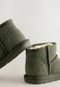 Kurze grüne Wildlederschuhe mit Schafslederfutter, runder Form, genähten Details und strukturiertem Gummisohlen, schräg positioniert.
