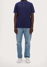 Námořnická modrá polo tričko se třemi knoflíky a náprsní kapsou, kombinované s světle modrými džíny a bílými teniskami. Jednoduchý, neformální design.