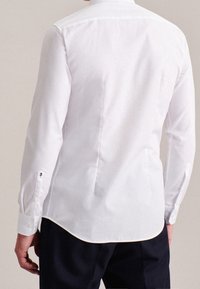 Camicia bianca con bottoni, maniche lunghe, taglio aderente, orlo arrotondato e piccolo motivo floreale sui polsini; tessuto dalla texture liscia.