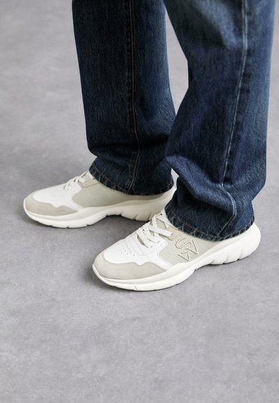 Baskets en gris clair et beige doux en maille avec des accents en daim. Dotées d'un design à lacets et d'une épaisse semelle en caoutchouc blanc. Portées avec un jean bleu.