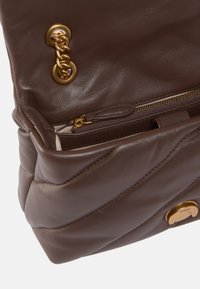 Borsa a mano in pelle marrone con design trapuntato, dettagli in catena dorata e una tasca con zip. L'interno rivela un ampio scomparto.