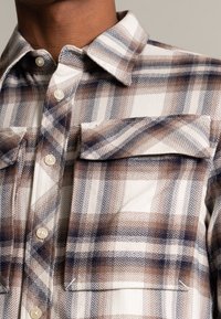 Skjorta i flanell i kräm, brun och marinblå rutmönster, med en strukturerad väv, knäppning och två bröstfickor med lock.