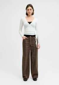 Biała, długa bluzka z długim rękawem, zapinana na kopertę z wiązaniem, zestawiona z brązowymi spodniami o szerokich nogawkach z wzorem wężowej skóry i czarnymi butami.