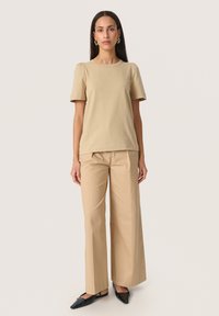 Beige kortærmet t-shirt lavet af bomuld, parret med brede beige bukser og sorte slip-on sko. Enkel halsudskæring og afslappet pasform.