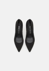 Pumps neri in suede con tacco alto e punta affusolata, foderati in pelle liscia, con il marchio "GUESS" sulle solette.