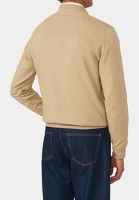 Giacca in morbido cotone beige con colletto a coste, progettata con un taglio rilassato e bordi rifiniti; abbinata a jeans in denim blu scuro.