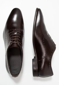 Chaussures habillées en cuir marron au cuir lisse, à bout pointu, à lacets et avec des perforations décoratives sur les côtés.