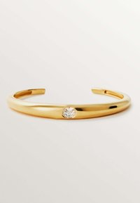 Pulsera de metal dorado con una superficie lisa y reflectante y un acento de gema ovalada clara en el centro.