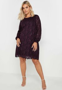 Vestido de encaje morado con mangas largas y abullonadas, dobladillo con forma de concha y patrones florales intrincados. Presenta una textura transparente y un ajuste cómodo.