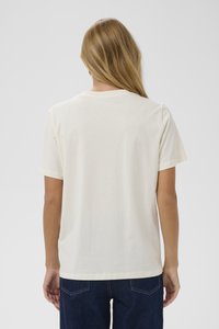 Camiseta de manga corta color beige claro con escote redondo. Tejido suave, corte relajado y diseño liso visible desde la parte de atrás. Combinada con jeans azul oscuro.