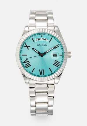 Hõbedane käekell ümmarguse korpuse, türkiissinise diali, mustade Rooma numbrite ja kuupäeva näidikuga. Omab poleeritud metallist käevõru ja soonel külge.