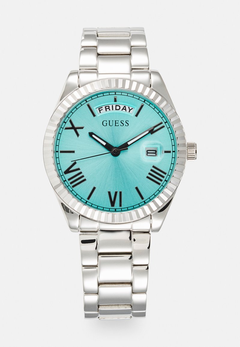 Ezüst karóra kerek tokban, türkiz számlappal, fekete római számokkal és dátumkijelzővel. Polírozott fém karkötővel és bordázott szegéllyel rendelkezik.