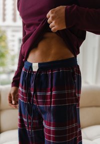 Gestreepte pyjamabroek in marineblauw en bordeauxrood met witte strepen, voorzien van een verstelbare tailleband met trekkoord. Langetermijn maroon top.