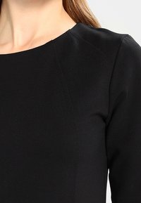 Musta pusero pyöreällä kauluksella, hienoilla ompelutiedoilla ja sileällä pinnalla. Omistaa istuvan siluetin ja pitkät hihat.