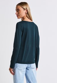 Donkerblauwe langslavige top met een ronde hals, een soepele textuur en een relaxte pasvorm. Lichte denim jeans met een eenvoudig ontwerp van een achterzak.