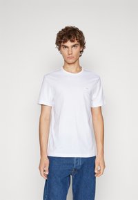 White cotton t-shirt with short sleeves, round neckline, fitted design, featuring a small brand logo on the left chest area.