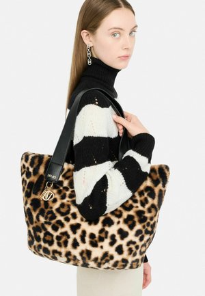 Borsa a spalla con stampa leopardata, texture morbida, manici in pelle nera e charm con logo. Modello che indossa un maglione a righe bianco e nero.