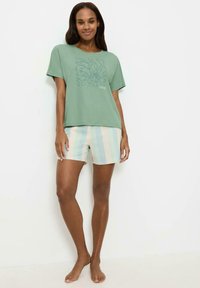 Zielony bawełniany T-shirt z kwiatowym nadrukiem, w połączeniu z jasnoniebieskimi i beżowymi spodniami w paski. Ubranie ma luźny krój i casualowy design.