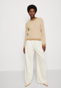Maglione a righe beige e bianche con orlo a costine, abbinato a pantaloni beige a gamba larga caratterizzati da righe verticali e tacchi nude a punta.