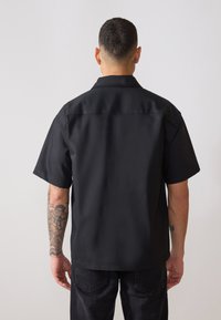 Μαύρο κοντομάνικο πουκάμισο με λεία υφή και κλασικό γιακά. Διαθέτει ίσια γραμμή και καθαρό, απλό σχέδιο.